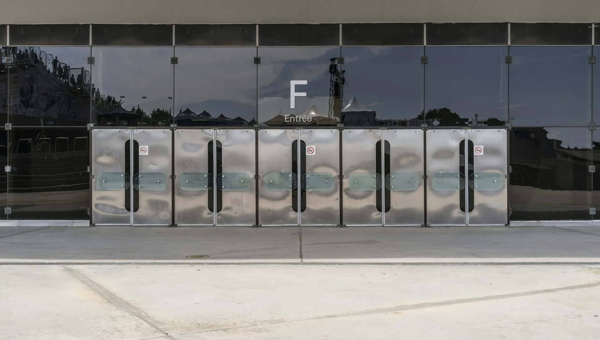 Metal entrance doors with long vertical handles beneath a reflective glass facade